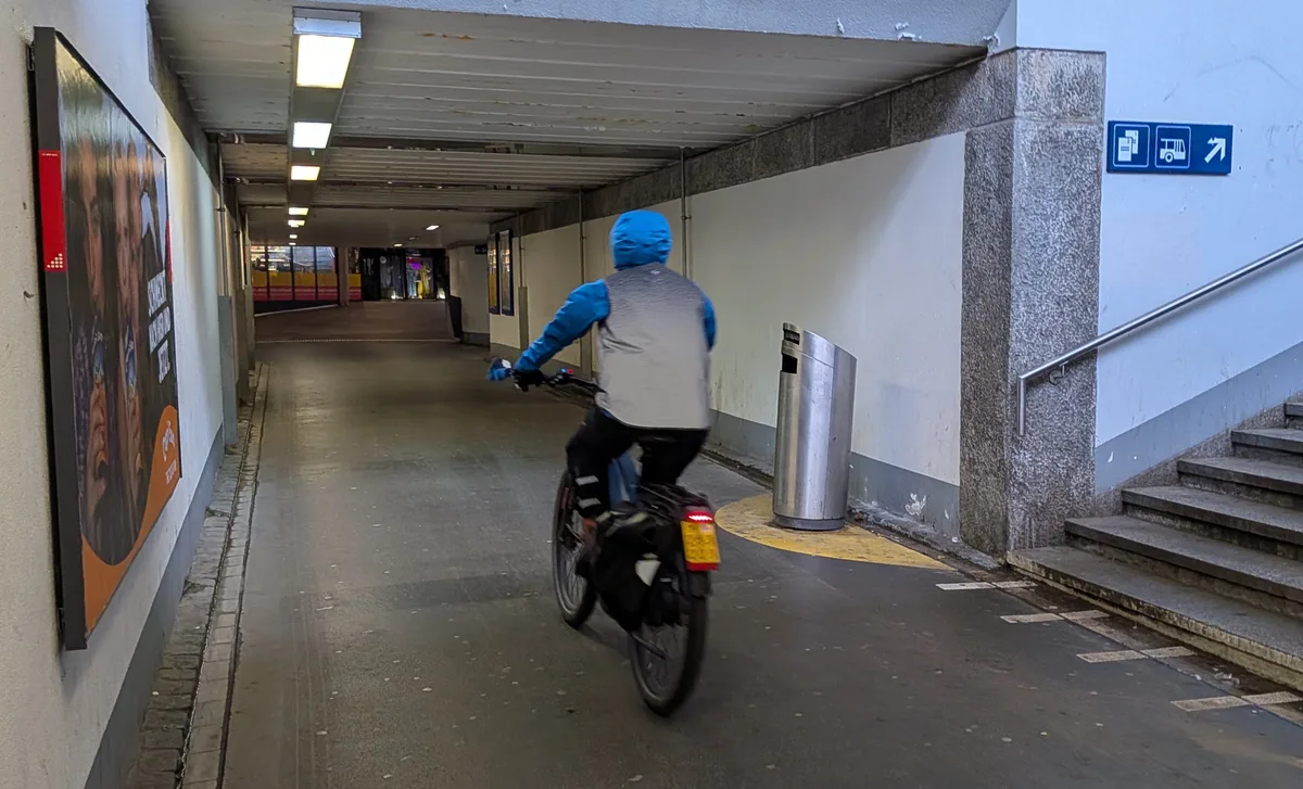 Man sieht eine düstere Bahnhofunterführung mit Passanten und Velofahrern.